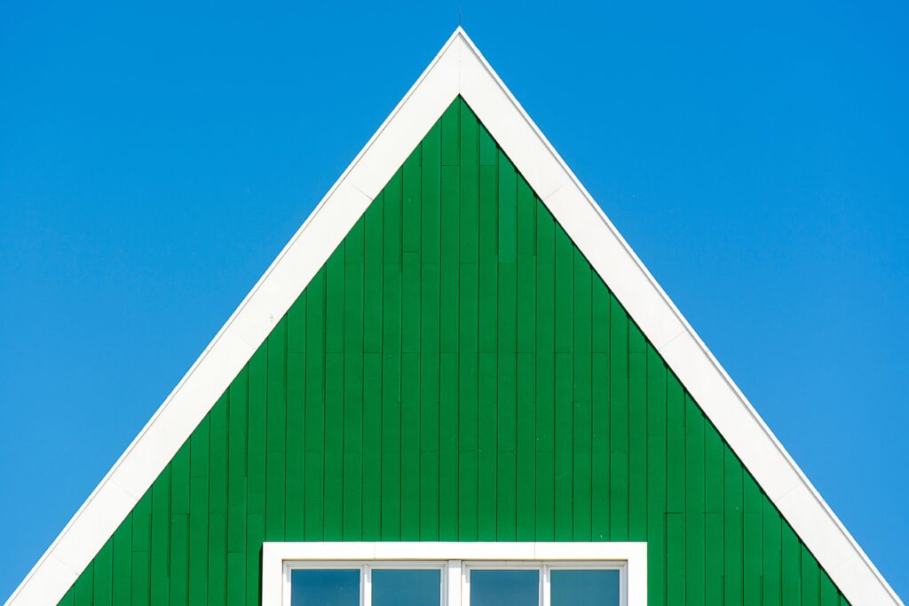 Minimalist green facade with triangular design and white outline, set against a clear blue sky in Zaandam, Netherlands.